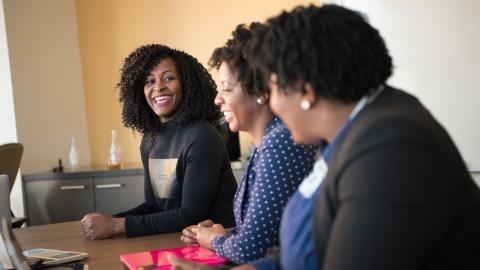 Three black women sitting next to a table, talking.